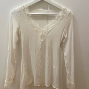 Vit långärmad topp med spetsdetaljer - Säljer denna eleganta vit långärmad topp med v-ringning och spetsdetaljer vid hals och ärmslut från Intimissimi!Perfekt för en stilren look. Säljer den för den tyvärr inte kommit till användning! Finns inga defekter då den aldrig använts förutom när jag testat den! Priset kan diskuteras vid snabb affär!!😊😊🌸