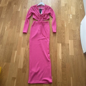 Rosa ribbad långärmad, cut out maxiklänning - Snygg rosa ribbad klänning som aldrig har använts, prislapp är fortfarande kvar! Långärmad topp som sitter ihop med snörning med en maxikjol