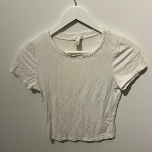 Vit ribbad croppad topp från Bozzolo - Säljer en vit ribbad croppad topp från Bozzolo. Toppen har korta ärmar och en rund halsringning, perfekt för en avslappnad stil. Tillverkad i ett mjukt och stretchigt material för extra komfort.