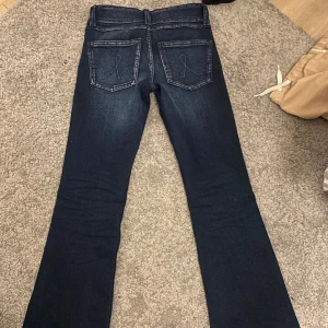 Mörkblå bootcut jeans - Snygga mörkblå bootcut jeans med klassisk femficksdesign och dubbla knappar i midjan. Perfekta för en avslappnad stil med en touch av retro. Passar bra till både sneakers och klackar.