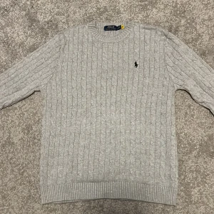 Grå stickad tröja från Polo Ralph Lauren - Stilren Ralph lauren cable knit. Fick i julklapp och säljer därför den inte passar längre. Passar runt längden 180+ och är i storlek M. Då jag fick den i julklapp kan jag inte stå för autenticiteten men med tanke på materialet och påsarna jag fick den i kan jag nog garantera äkthet. Endast använd en gång! Tveka inte att höra av er vid frågor. Prutning går nog bra!