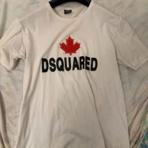 Vit t-shirt från Dsquared2 - Snygg vit t-shirt från Dsquared2 med ett rött lönnlöv och svart text på bröstet. Perfekt för en stilren och avslappnad look.