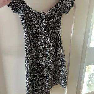 Svartvit blommig klänning - Säljer en söt svartvit blommig klänning. Klänningen har korta ärmar och en smockad överdel som ger en fin passform. Perfekt för en somrig look! 🌸