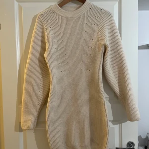 Crémevit stickad klänning - Mysig crémevit stickad klänning med långärmad design. Perfekt för kyligare dagar med sin varma och bekväma passform. Den har ett enkelt men stilrent mönster som ger en extra touch och kramar om kroppen på ett fint sätt.