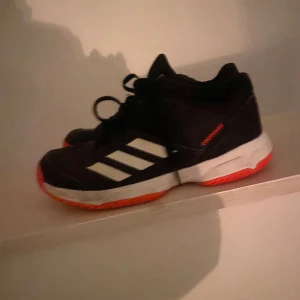 Svarta Adidas sneakers med orange sula - Snygga svarta Adidas sneakers med vita ränder och en iögonfallande orange sula. Perfekta för en sportig look med bekväm passform och snörning för justering.