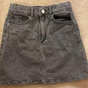 Grå jeanskjol från h&m - Snygg grå jeanskjol från &Denim i en klassisk design med fem fickor och knappgylf. Kjolen har en rak passform och är perfekt för en avslappnad stil. Tillverkad i Pakistan.