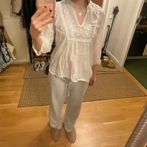 Vit blus med broderade detaljer - Säljer en luftig vit blus med v-ringning och broderade detaljer framtill. Blusen har trekvartsärmar och en avslappnad passform.