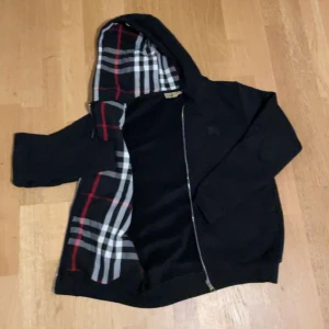 Svart burberry hoodie  - Snygg svart hoodie från märket burburry med dragkedja och huva. Insidan har ett klassiskt rutigt mönster i rött, vitt och grått. Perfekt för en casual look med stil. Säljer då jag inte diggar den längre, använt sparsamt. Skriv vid frågor eller funderingar!😊