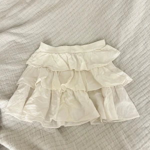Vit volangkjol - Charmig vit kortkjol med flera lager av volanger. Perfekt för en somrig look med sin luftiga design. Kjolen har en elastisk midja för bekväm passform. Står ej storlek men skulle gissa på S/XS💕💕