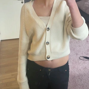 Vit ribbad kofta med knappar - Säljer en stilren vit kofta med ribbad struktur och stora knappar framtill. Koftan har en croppad passform och långa ärmar, perfekt för lager-på-lager-stil. Passar både till jeans och kjol för en avslappnad look.