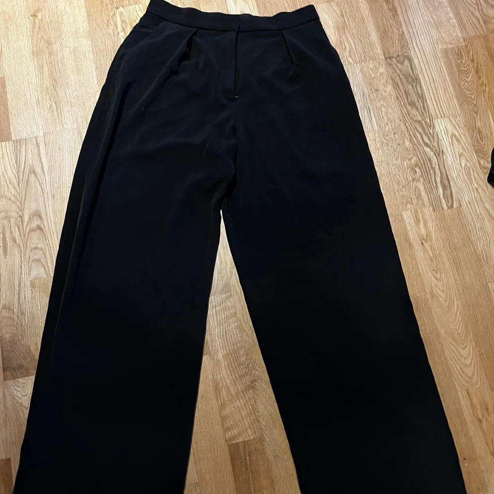 Snygga svarta kostymbyxor med hög midja och en klassisk rak passform. Perfekta för en stilren look. Byxorna har en diskret dragkedja framtill.. Farkut & Housut.