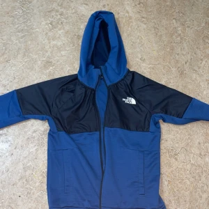 Svart blå Tracksuit från the north face ( pris kan diskuteras) - Säljer en snygg blå och svart jacka från The North Face med huva och dragkedja. Jackan har en cool design med svarta paneler och The North Face-logga på bröstet. Perfekt för kyligare dagar! 