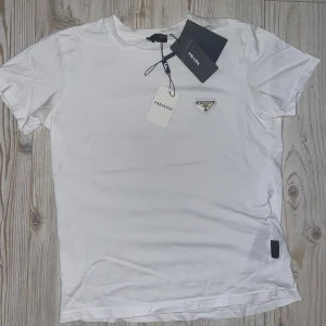 PRADA T-SHIRT - Säljer en Prada T-shirt i mycket bra skit. Använd 3-4 gånger annars tyckte jag att det inte var min stil riktigt. Annars en skön T-shirt nu till sommaren. Tveka inte på att ställa frågor och lägga ett prisförslag!