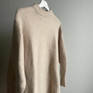 Beige stickad klänning från H&M - Säljer en mysig beige stickad klänning från H&M. Klänningen har en klassisk rund halsringning och långa ärmar, perfekt för kyligare dagar. Den är enkel och stilren, vilket gör den lätt att matcha med olika outfits. Använd men i fint skick!