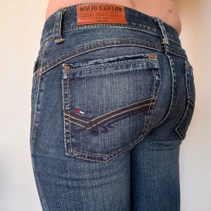 Blå jeans från Hilfiger Denim - Snygga blå jeans från Hilfiger Denim med klassisk femficksdesign och broderad logga på bakfickan. De har en knappgylf och bälteshällor, perfekt för en avslappnad stil.