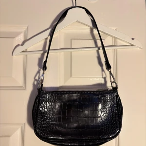 Svart axelväska med krokodilmönster - Snygg svart axelväska med krokodilmönster och dragkedja. Perfekt för att ge din outfit en trendig touch.