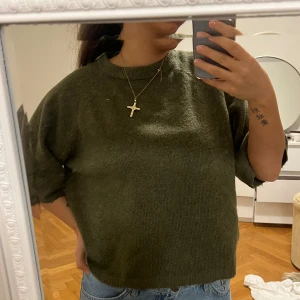 Olivgrön stickad tröja - Säljer en olivgrön stickad tröja med korta ärmar. Tröjan har en avslappnad passform och är perfekt för en stilren vardagslook. Den är enkel att matcha med jeans eller kjol.