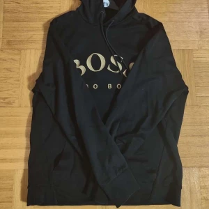 Hugo Boss hoodie  - Säljer en Elegant Hoodie från Hugo Boss i storlek L, Svart med guld text som ger en lyxig touch, Väldigt bra skick (som ny), PRIS KAN DISKUTERAS 