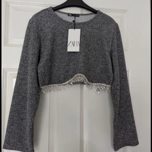 Grå croppad tröja Zara - Säljer en superfin grå croppad tröja från Zara. Detaljerad med glitter längs nederkanten. Tröjan är endast använd en gång