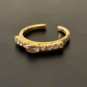 Guldfärgad ring med stenar - Elegant guldfärgad ring prydd med gnistrande stenar. Perfekt för att ge en touch av glamour till din stil. Den har en öppen design som gör den justerbar och bekväm att bära.