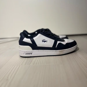 Svartvita sneakers från Lacoste - Snygga svartvita sneakers från Lacoste med klassisk design. Skorna har snörning och Lacoste-loggan på sidan. Perfekta för en stilren look. Knappt använd 