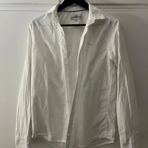 Vit skjorta från Hampton Republic - Säljer en stilren vit skjorta från Hampton Republic. Skjortan har långa ärmar och knappar framtill. Perfekt för en klassisk look. Passar till många olika tillfällen och stilar. Nästan oanvänd