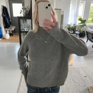 Grå stickad tröja - Säljer en stilren grå stickad tröja med långa ärmar och ribbade detaljer vid ärmslut och nederkant. Perfekt för kyligare dagar och enkel att matcha med olika outfits.