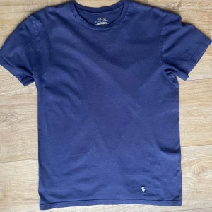 Mörkblå t-shirt från Polo Ralph Lauren - Säljer en stilren mörkblå t-shirt från Polo Ralph Lauren. Den har en klassisk passform med korta ärmar och är tillverkad i mjuk bomull. Den ikoniska loggan är diskret broderad i vitt på framsidan. Perfekt för en avslappnad look.