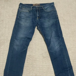 Blå jeans från Giordano - Snygga blå jeans från Giordano med en low-rise passform och tapered stil. De har klassiska fem fickor och en knappgylf. Perfekta för en avslappnad look.