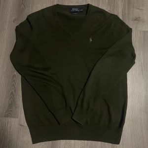   Ralph Lauren tröja grön - Säljer en stilren grön tröja från Polo Ralph Lauren i pima bomull. Tröjan har en v-ringad design och är långärmad med en broderad logotyp på bröstet. Perfekt för en klassisk look. 