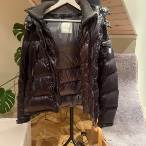 Moncler jacka - Snygg svart dunjacka från Moncler med glansig finish och klassisk pufferdesign. Jackan saknar en dragkedja till västen på insidan och har en liten flaw längst fram på armen.