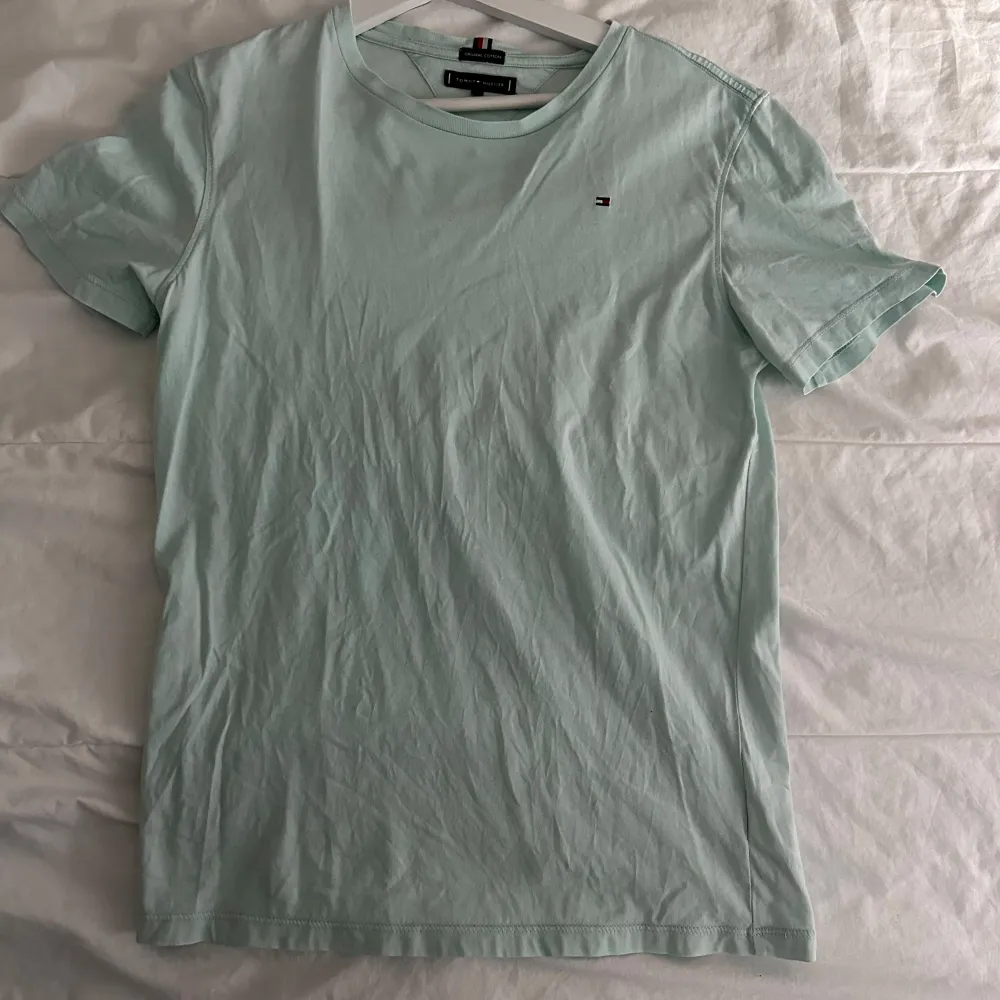 Säljer en stilren ljusgrön t-shirt från Tommy Hilfiger i ekologisk bomull. T-shirten har en liten broderad logga på bröstet och rund halsringning. Perfekt för en avslappnad look.. T-paidat.