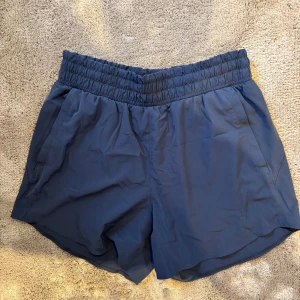 Blå träningsshorts från Under Armour - Blås under armour träningsshorts med fickor på varje sida. Shoetsen har en elastisk midja och snörning för perfekt passform. 