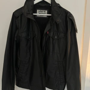 Svart jacka från Levi's - Snygg svart fodrad regn/vind jacka från Levi's med luva som går att vecka ut och in