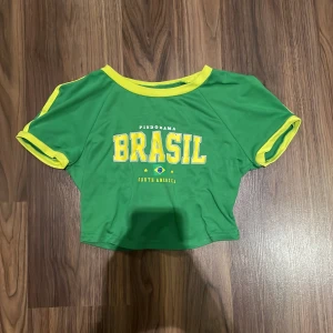 Topp  - Säljer en t-shirt topp från SHEIN I storlek S. Toppen har en tajt passform och är en kortare modell. Den är grön med gula detaljer och text framtill. Materialet är mjuk bomull 💕den är även något nopprig men inget man tänker på💕