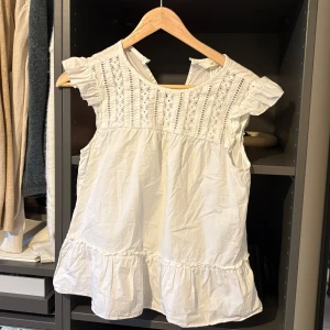 Vit blus från H&M - Söt vit blus från H&M med spetsdetaljer och volang vid ärmslut och nederkant. Perfekt för en somrig look med sina korta ärmar och luftiga design. Passar bra till både jeans och kjol för en avslappnad stil. Den är köpt utomlands och är använd en eller max två gånger så den är nästan ny 