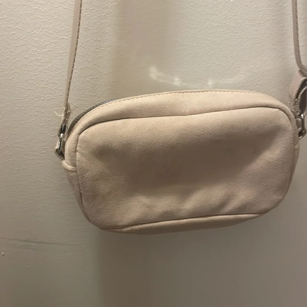 Snygg beige axelväska med flera praktiska fack och dragkedjor. Perfekt för att hålla ordning på dina saker. Väskan har en justerbar axelrem och är tillverkad i ett mjukt material.. Laukut & Käsilaukut.