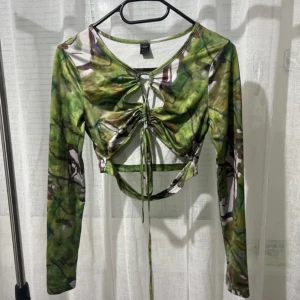 Grön camouflagemönstrad topp - Snygg grön camouflagemönstrad topp med långa ärmar och knytning framtill. Toppen har en unik design med öppna detaljer och är croppad för en trendig look.