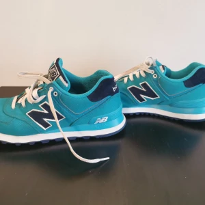 Turkosa sneakers från New Balance - Säljer ett par snygga turkosa New Balance 574 sneakers med vita snören och detaljer i mörkblått. Skorna har en klassisk design med märkets logga på sidan och en bekväm sula för vardagsbruk.