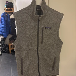 Grå fleeceväst från Patagonia - Säljer en grå fleeceväst från Patagonia med dragkedja framtill och praktiska fickor. Perfekt för lager-på-lager under kyliga dagar. Västen har en stilren design med en liten logotyp på bröstet. Storlek S och passar runt 170-180cm. Fint skick inga defekter. Nypris cirka 1200kr säljs för endast 679kr