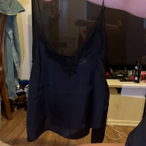 Svart linne med spetsdetaljer - Snyggt svart linne med tunna axelband och vacker spetsdetalj vid halsringningen. Perfekt för en stilren look.