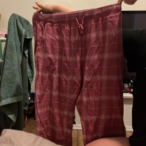 Rosa rutiga byxor med snörning - Säljer ett par bekväma rosa byxor med rutigt mönster. Byxorna har en elastisk midja med snörning för justerbar passform. Perfekta för en avslappnad stil.