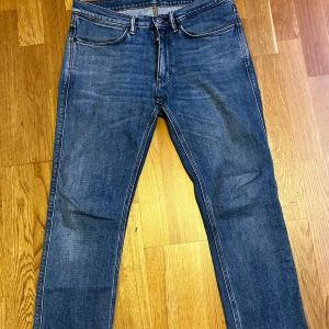 Acne Studios Jeans - Snygga blå jeans från Acne Studios 30x32 i en klassisk straight fit. De har en midwaist design och är tillverkade i bomull med en liten del elastan för extra komfort. Perfekta för en stilren look med sina enkla detaljer och diskreta bakfickor.