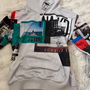 Flerfärgad hoodie från NA-KD - Säljer en cool flerfärgad hoodie från NA-KD med grafiskt tryck i olika färger som svart, blå, röd och grön. Hoodien har en stor ficka framtill och justerbar huva med dragsko 