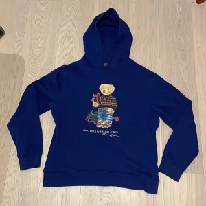 Blå hoodie från Ralph Lauren - Säljer en snygg blå hoodie från Ralph Lauren med en söt björn på framsidan. Perfekt för en avslappnad stil. Hoodien har långa ärmar och en klassisk huva. Passar perfekt för kyligare dagar. Det är XL junior men motsvarar ungefär vuxen S