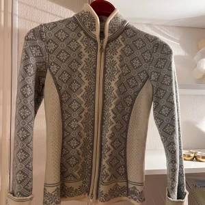 Så fin ljusblå och vit mönstrad kofta från Dale of Norway - Säljer en elegant grå och vit kofta från Dale of Norway med ett traditionellt mönster. Koftan har en dragkedja framtill och långa ärmar. Perfekt för kyliga dagar. Den är i 100% merinoull. Nypris på den var över 4499:- använd max 7ggr. 