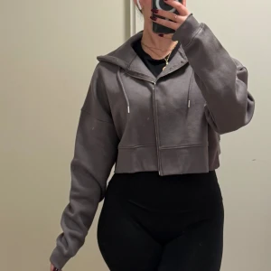 Grå croppad hoodie - Säljer en grå croppad hoodie med dragkedja och huva. Den har långa ärmar och en avslappnad passform, perfekt för en casual look. Hoodien är både stilren och bekväm.