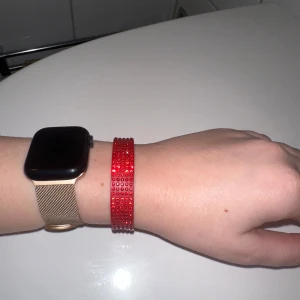 Rött swarovski armband med glittriga detaljer - Snyggt rött armband från Swarovski med glittriga detaljer som ger en extra touch till din outfit. Armbandet har en enkel knäppning och är perfekt för att lägga till lite färg och stil.
