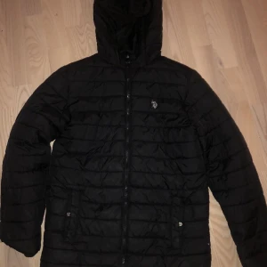 Polo jacka - Polo jacka Säljer en svart quiltad dunjacka med huva. Jackan har dragkedja framtill och två fickor med knappar. Perfekt för kyliga dagar. 🖤