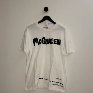 Alexander McQueen T-shirt  - Snygg vit t-shirt från Alexander McQueen med stort svart tryck 'McQueen' på framsidan. T-shirten har en klassisk rund hals och korta ärmar. Perfekt för en stilren och modern look. Kvitto från Vestiaire finns, den är endast testad med tags på! Hör gärna av er vid flera frågor eller funderingar!🌟💯